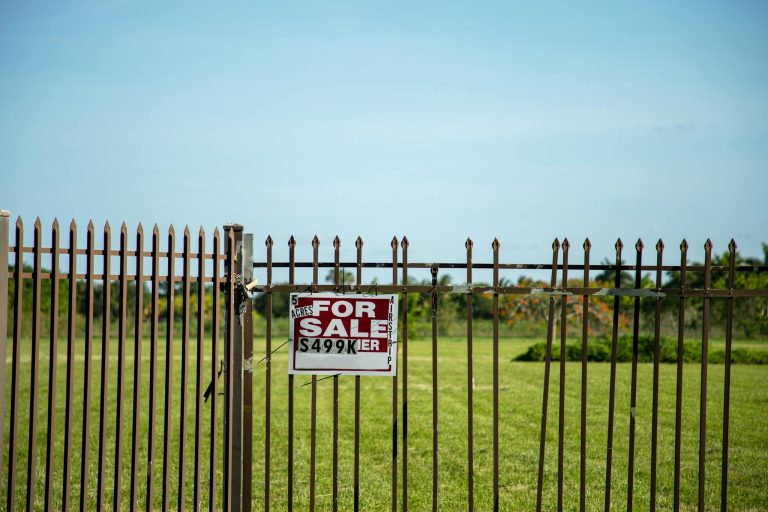 A large plot of land bordered by an iron fence, complete with a 'For Sale' sign in Miami, FL. Ideal for development.