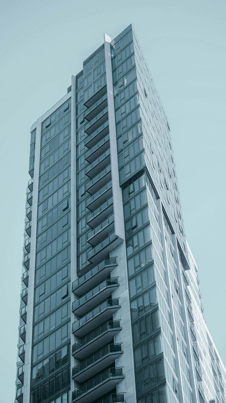 A sleek high-rise building featuring a modern glass facade against a clear blue sky.