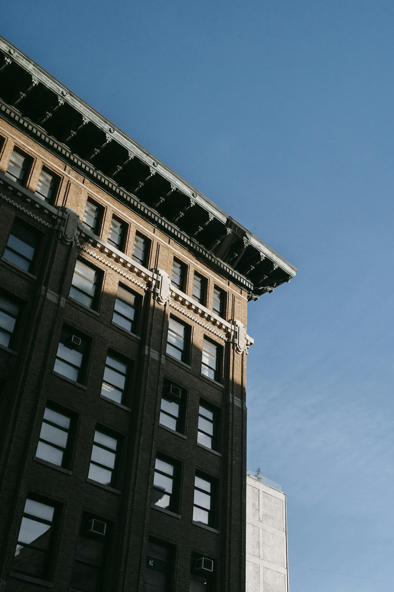 From below of corner of apartment building with roof cornice located against blue sky in city on street in sunlight