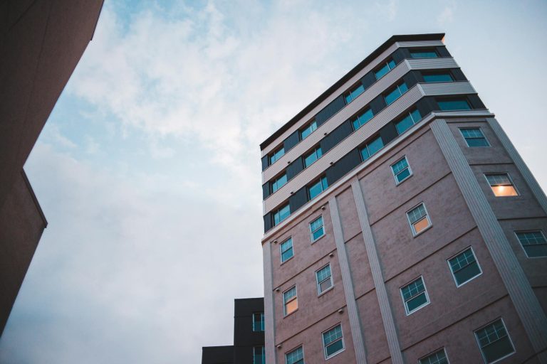 Low angle view of a modern multi-story building with glass windows against a blue sky.